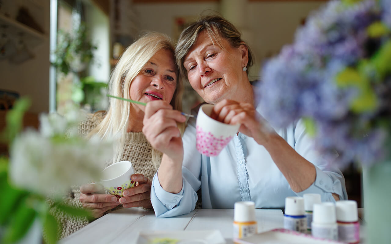 Two older women, one painting a teacup