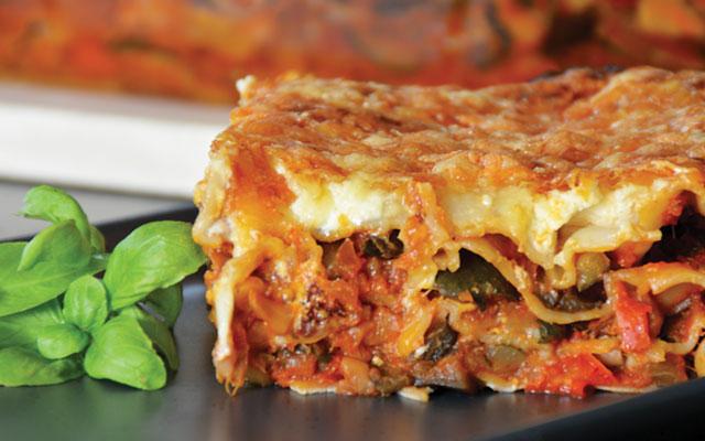 A slice of lasagna garnished with a spring of basil leaves